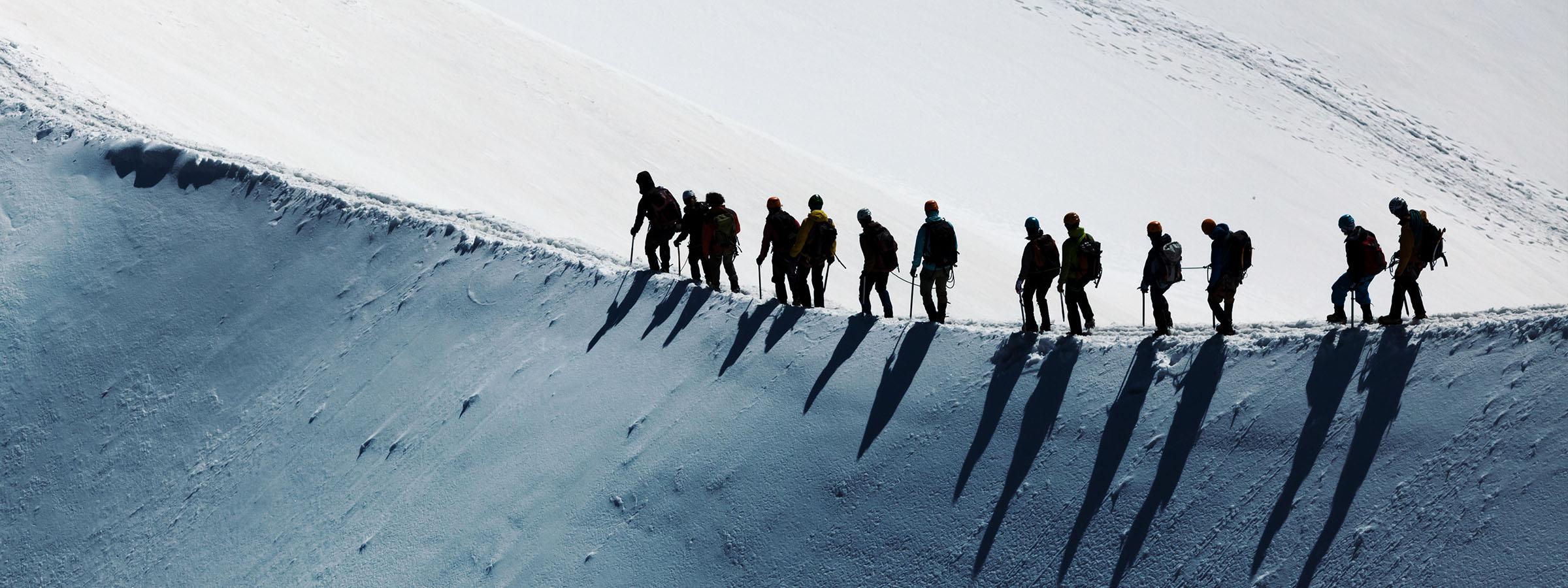 Mountain climbers walking along a snowtop ridge.