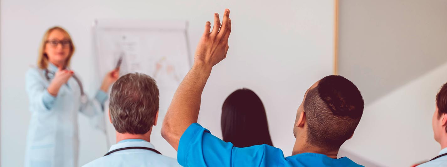 Healthcare student in class with hand raised to