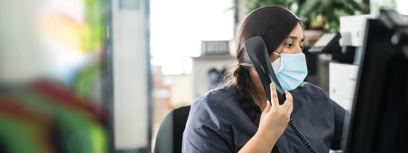 Healthcare receptionist with mask on speaking to a patient on the phone