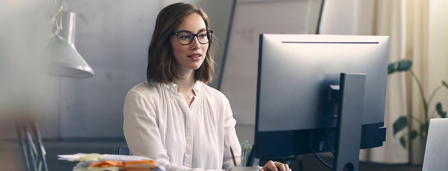 A woman wearing glasses views a monitor screen