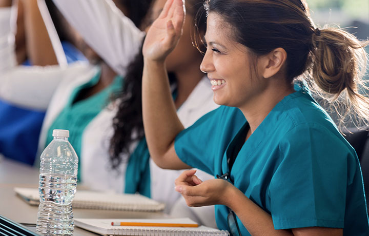 image of a smiling young latina woman in scrubs raising her hand