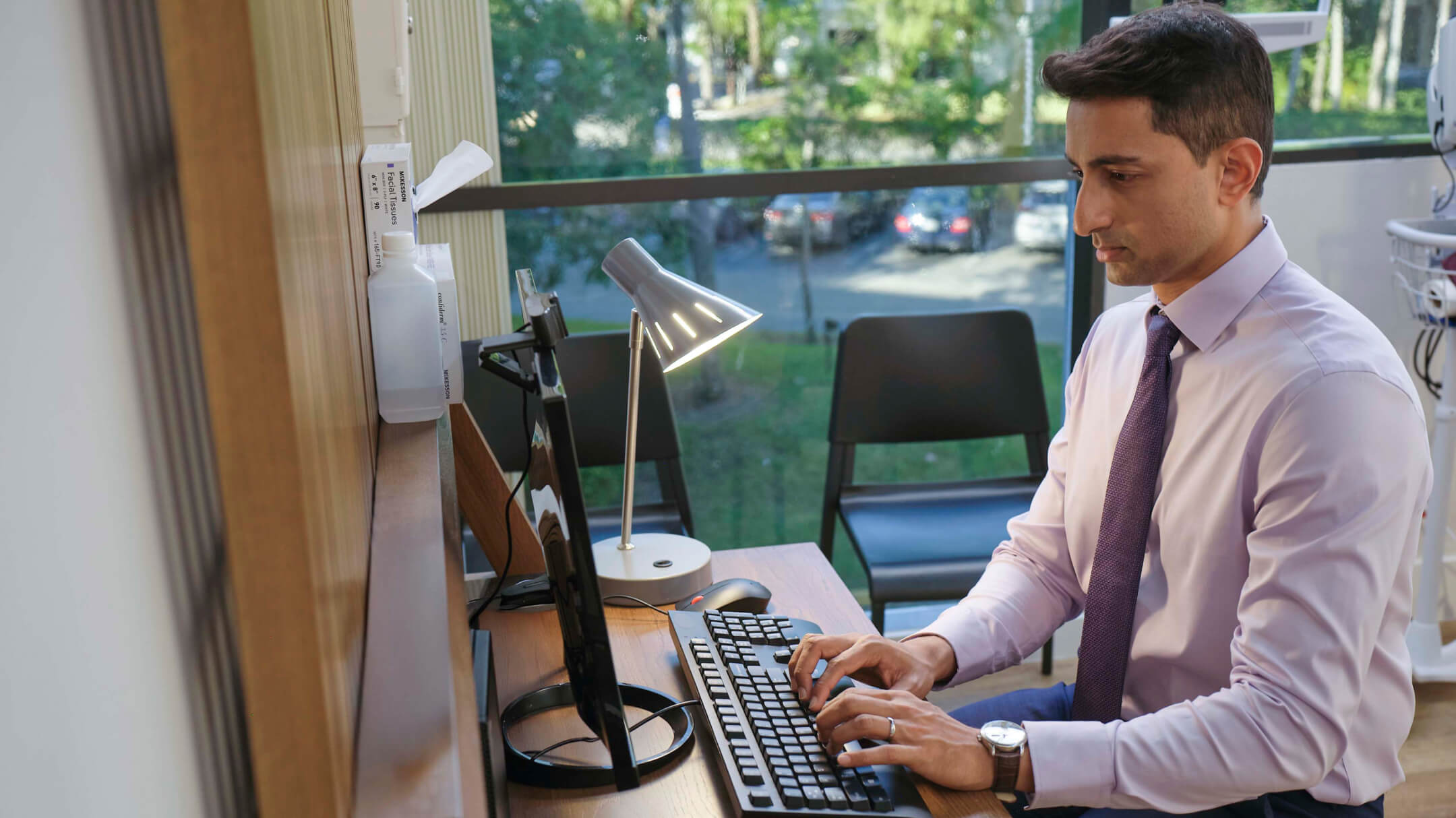 Clinician sitting at a desk working on a computer to coordinate care between clinics and ASCs.