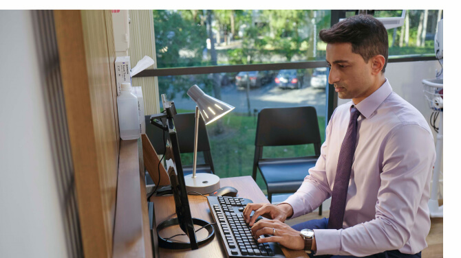 Clinician sitting at a desk working on a computer to coordinate care between clinics and ASCs.
