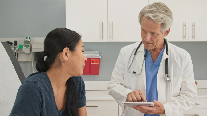 A doctor discusses health concerns with a patient in a hospital room, emphasizing person-centered care.