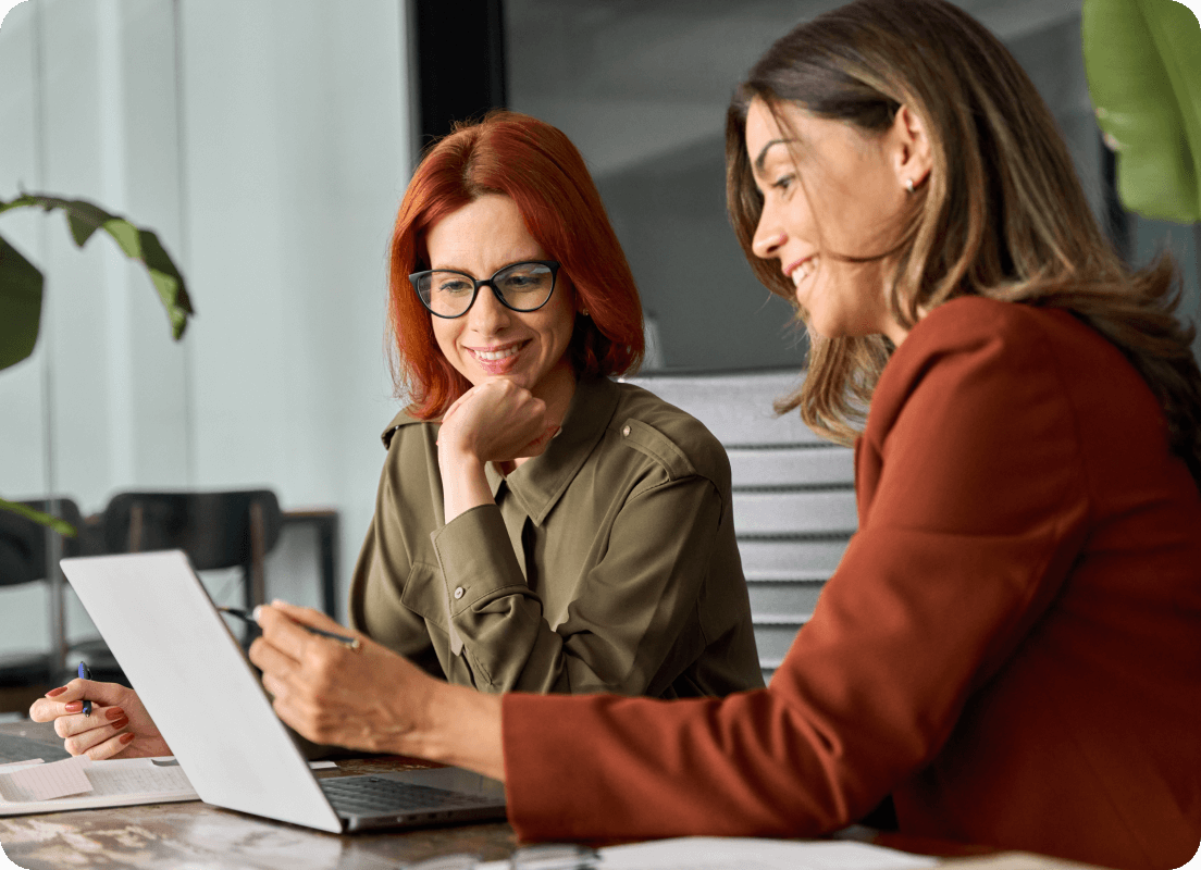 Two women smiling and reviewing display from an open laptop