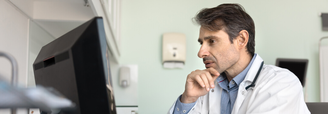 Physician sitting at desk in front of monitor.