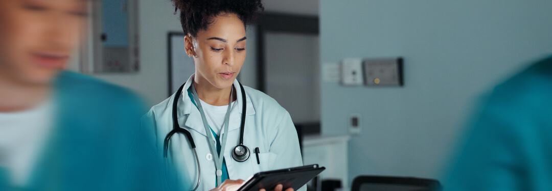 Physician standing in a clinical setting working on a tablet with AI tools.