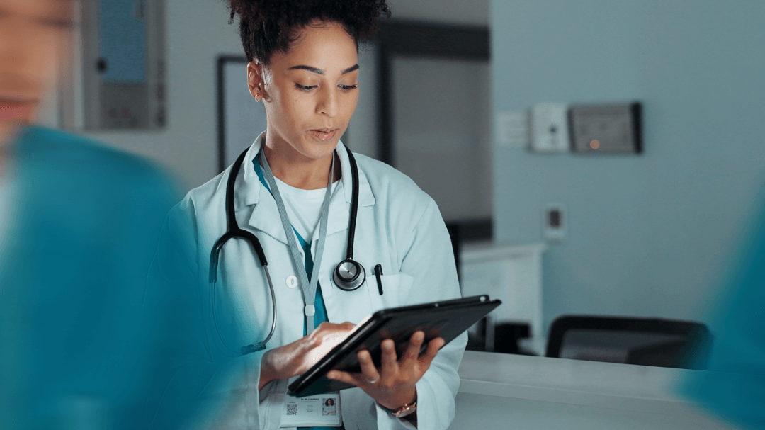 Physician standing in a clinical setting working on a tablet with AI tools.  