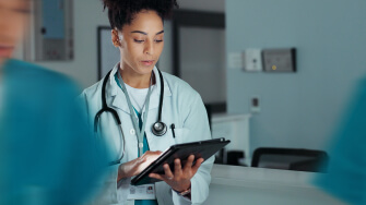Physician standing in a clinical setting working on a tablet with AI tools.  