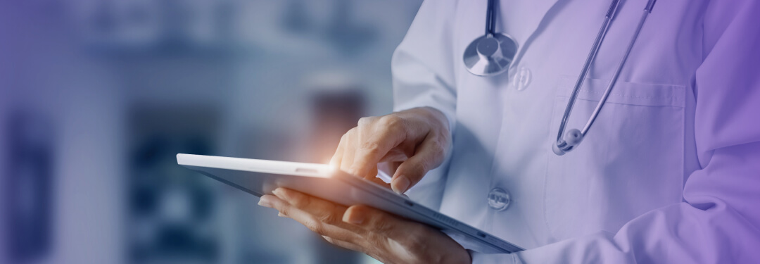 A physician wearing a stethoscope and white coat uses iPad.