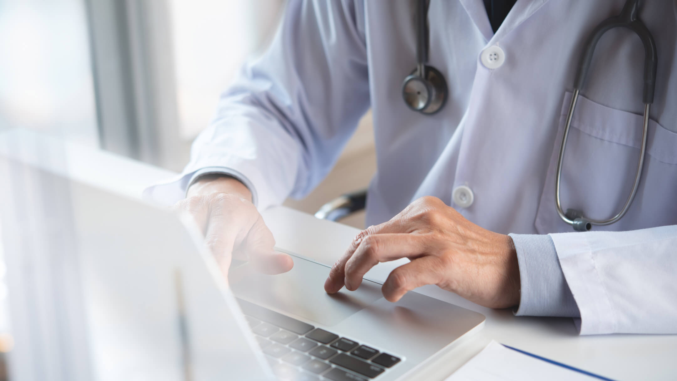 A physician typing on a laptop, highlighting the connection of global software to local healthcare through Agentic AI technology.
