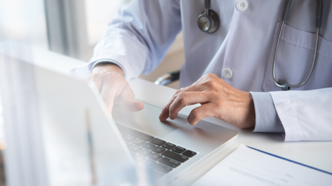 A physician typing on a laptop, highlighting the connection of global software to local healthcare through Agentic AI technology.