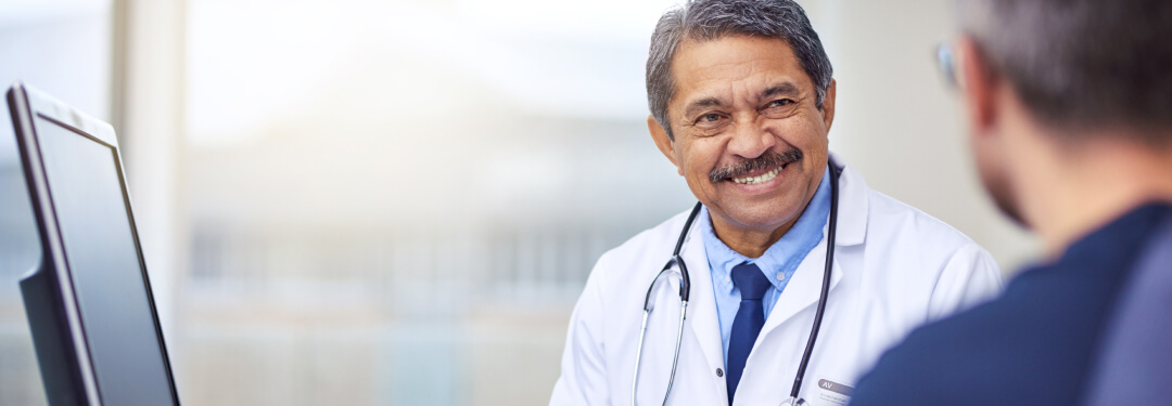 Doctor smiles while sitting and speaking with a patient following an exam.