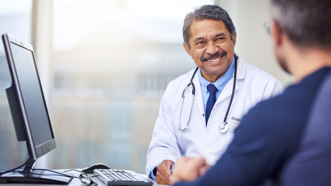 Doctor smiles while sitting and speaking with a patient following an exam.