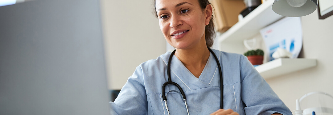 A physician works at a desk with a laptop, exploring EHR selection pitfalls for her practice.