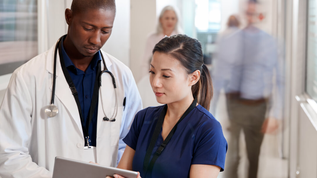 A doctor and a nurse examine a tablet together, sharing insights on patient care in a healthcare facility.