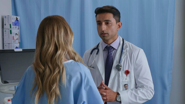 Physician wearing a white coat speaking with a patient in exam room