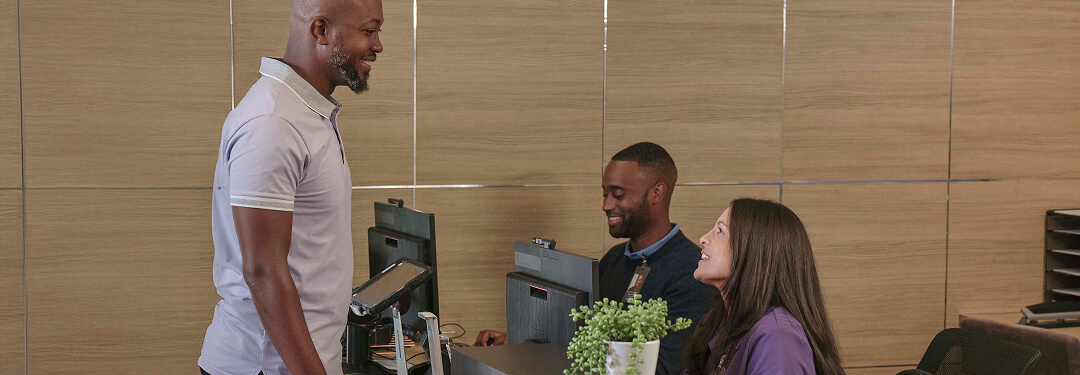 Patient standing at the reception desk at an ASC engaging with the two staff members working behind the counter.
