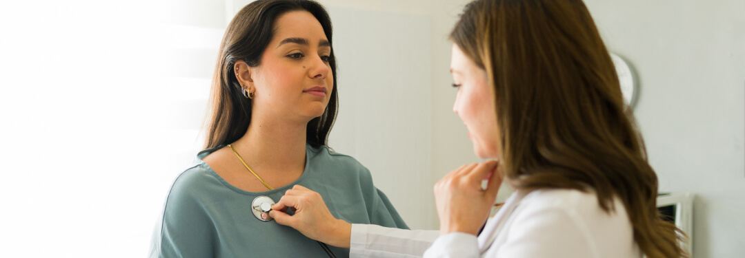 A physician uses a stethoscope to monitor the heart rate of patient in a medical setting.