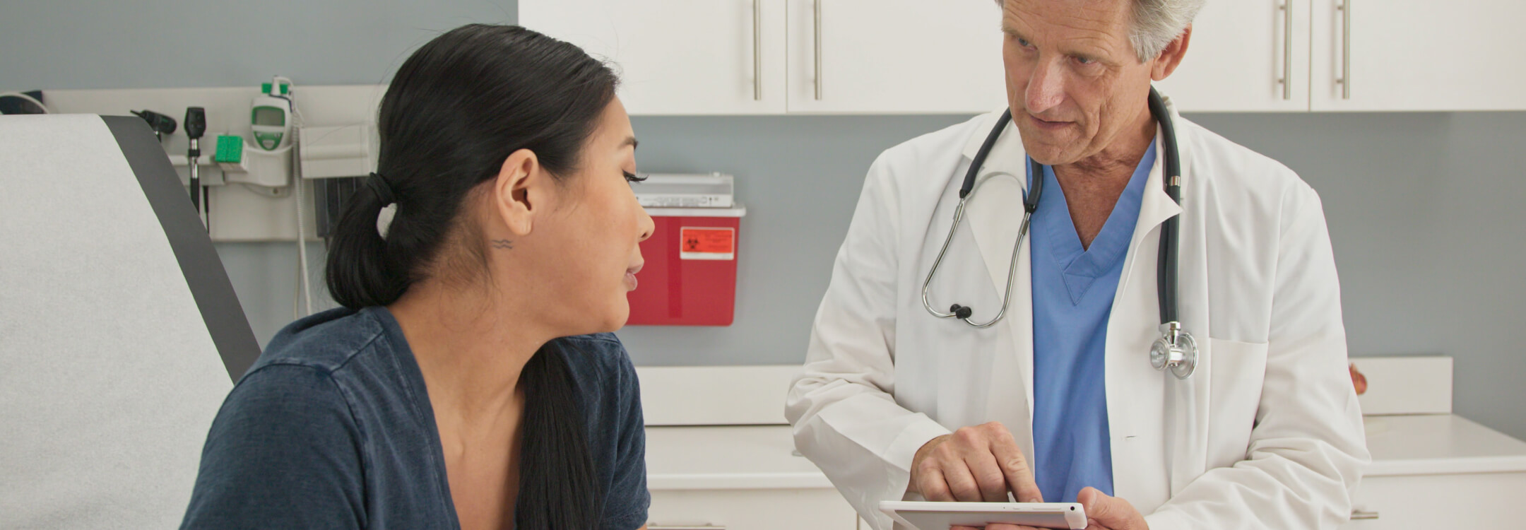 A doctor discusses health concerns with a patient in a hospital room, emphasizing person-centered care.