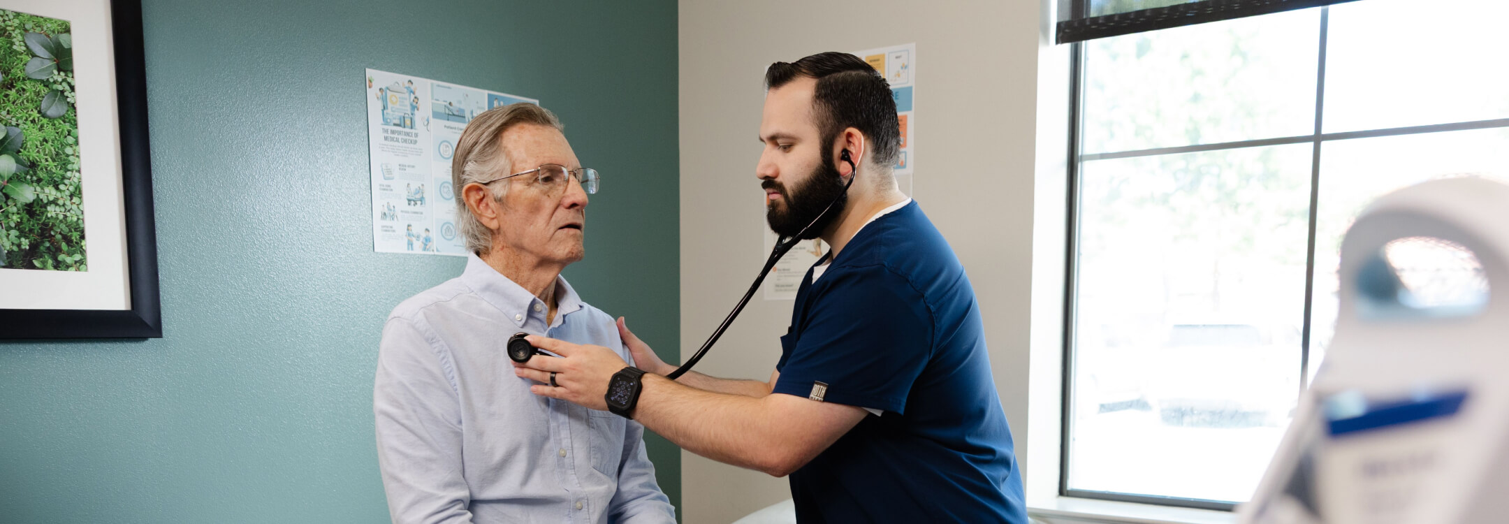 A healthcare professional uses a stethoscope to listen to patient's chest during a medical exam in a clinic room.