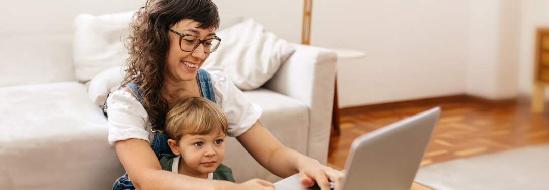 A woman uses her laptop computer to send a message to her physician’s office as her young son looks on.