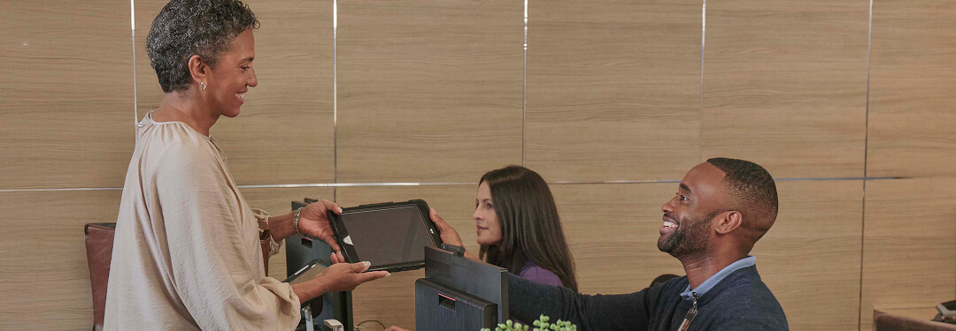 At the front desk, a patient gives a tablet to an admin, showcasing innovative digital patient check-in solutions.