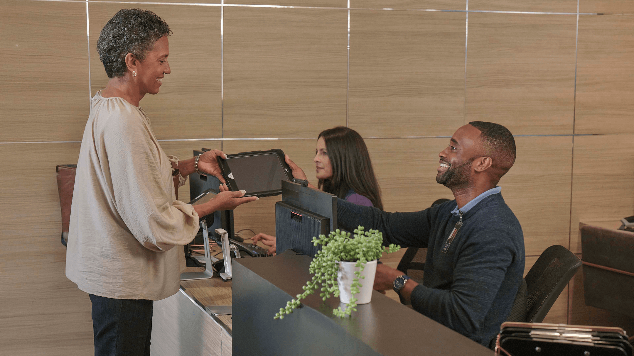 At the front desk, a patient gives a tablet to an admin, showcasing innovative digital patient check-in solutions.