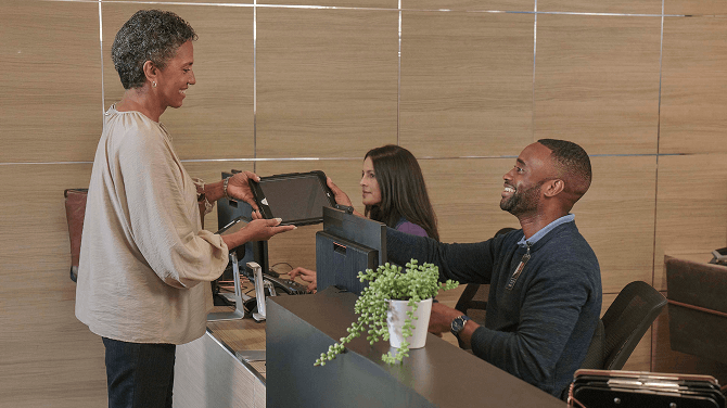 At the front desk, a patient gives a tablet to an admin, showcasing innovative digital patient check-in solutions.