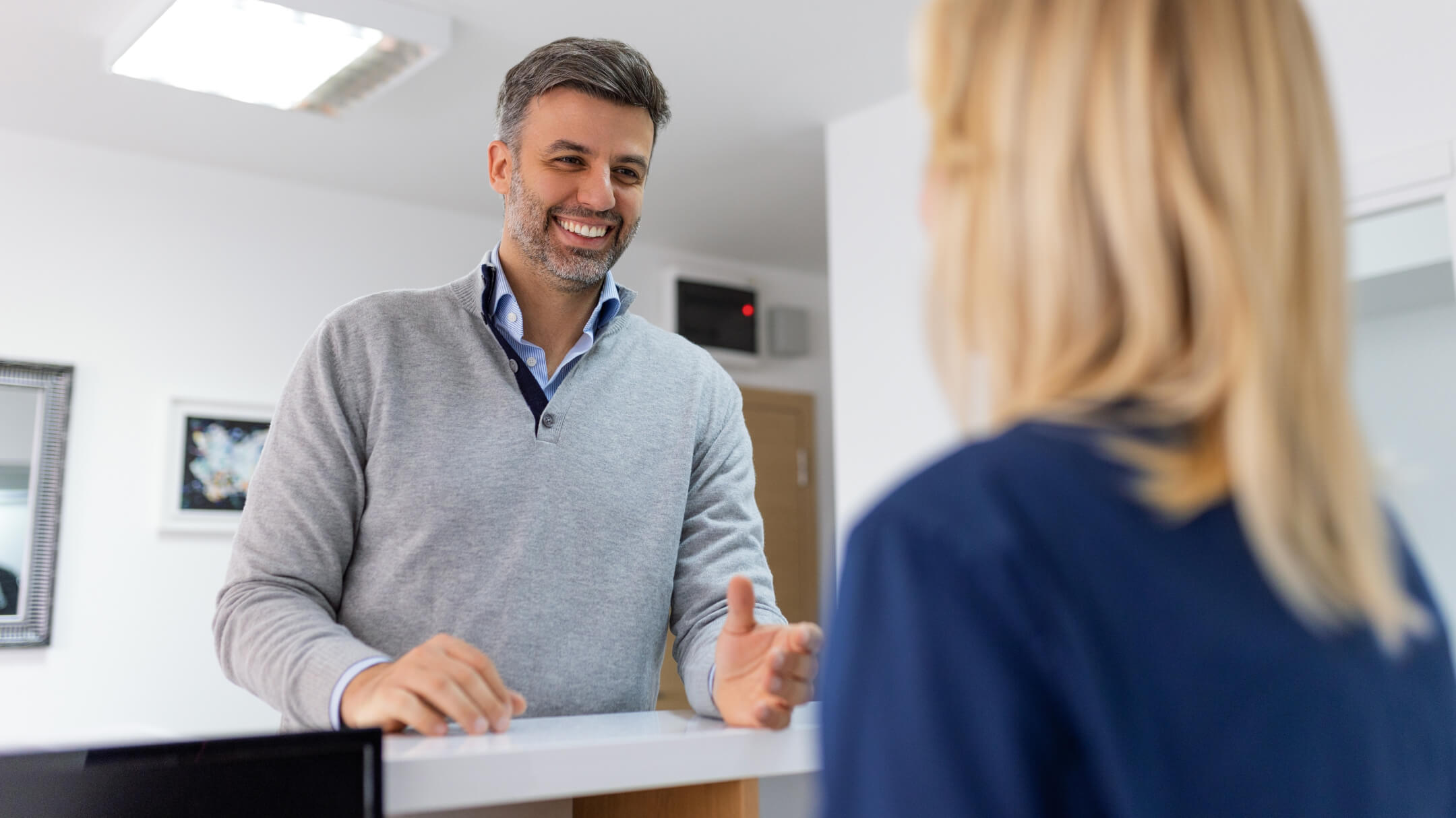  A patient and an admin discuss at a desk, highlighting the importance of direct payer integrations with EHR systems for practices.