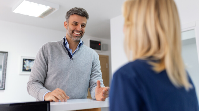 A patient and an admin discuss at a desk, highlighting the importance of direct payer integrations with EHR systems for practices.