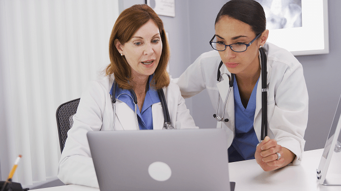 Two physicians collaborate over a laptop, discussing key features for future-proofing EHR selection.