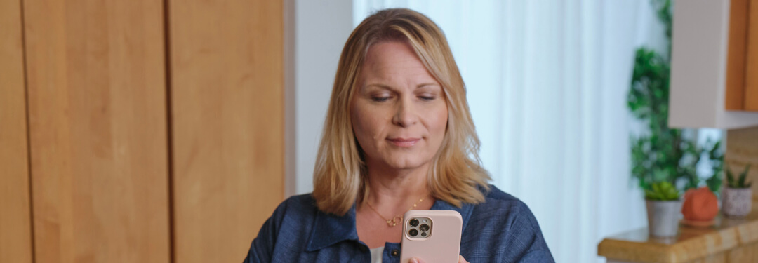 A woman looks at her smartphone using digital self check-in to enhance patient engagement.