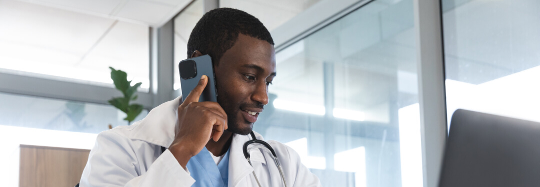 A physician talks on a mobile phone while looking at a computer screen.