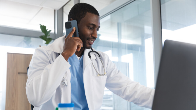 A physician talks on a mobile phone while looking at a computer screen.