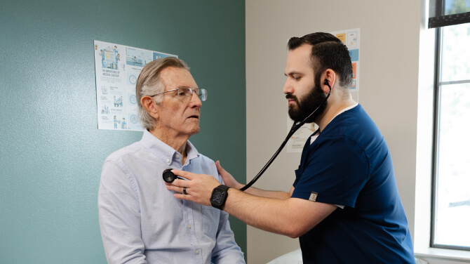 Doctor checking a patient's heart rate with a stethoscope in a clinical setting.
