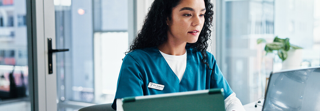 A nurse uses her laptop, utilizing ambient AI for documentation and medical billing tasks in a healthcare setting.
