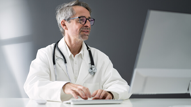 A professional medical provider working at a computer in a clinical office setting representing athenahealth's EHR integration efforts.