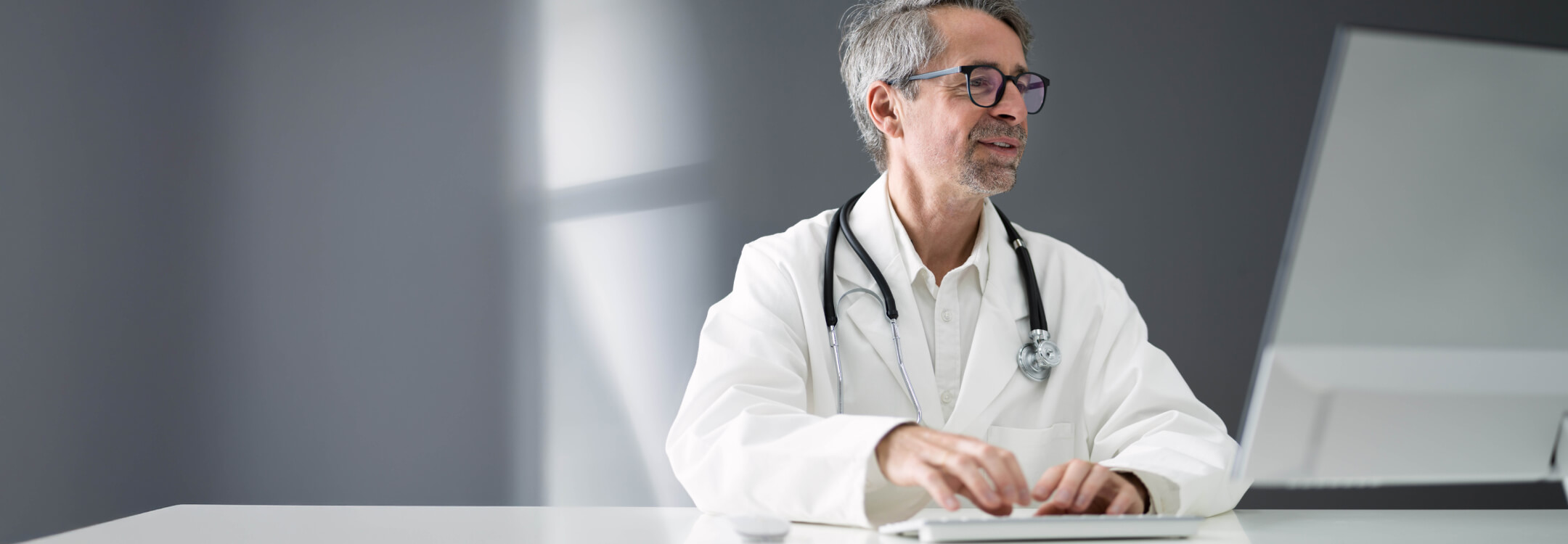 A professional medical provider working at a computer in a clinical office setting representing athenahealth's EHR integration efforts.