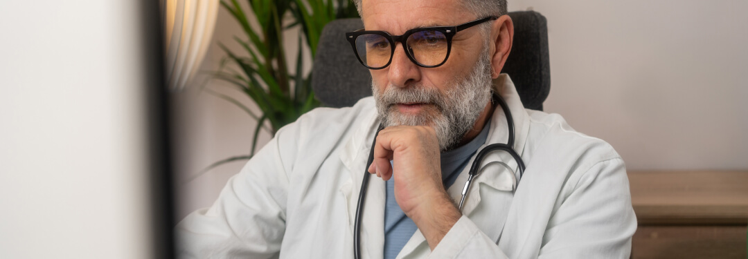 The doctor seated at the computer is focused on cybersecurity under the HIPAA Privacy Rule.
