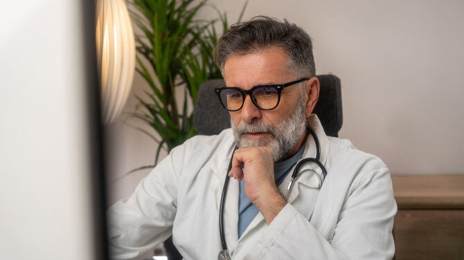 The doctor seated at the computer is focused on cybersecurity under the HIPAA Privacy Rule.