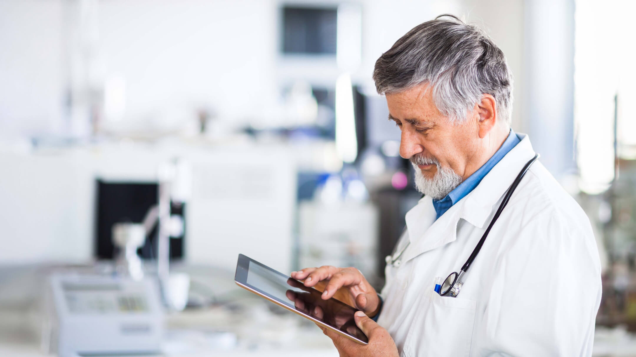 Male physician holding a tablet to review patient records on an interoperable platform.