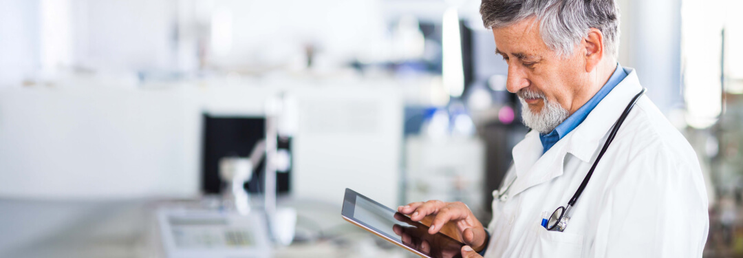 Male physician holding a tablet to review patient records on an interoperable platform.