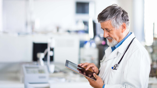 Male physician holding a tablet to review patient records on an interoperable platform.