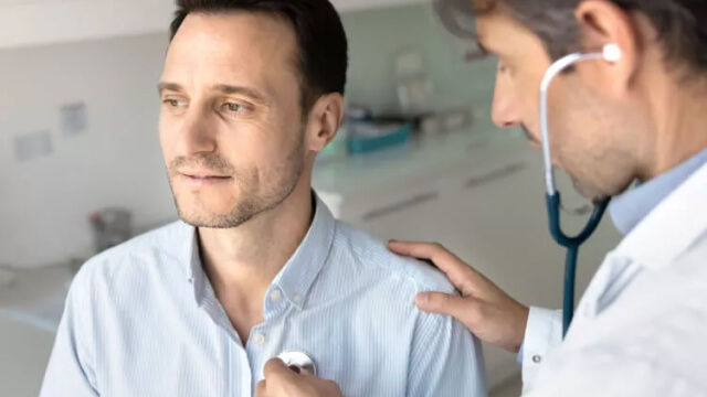 Physician listens to patients heartbeat through stethoscope in an exam room