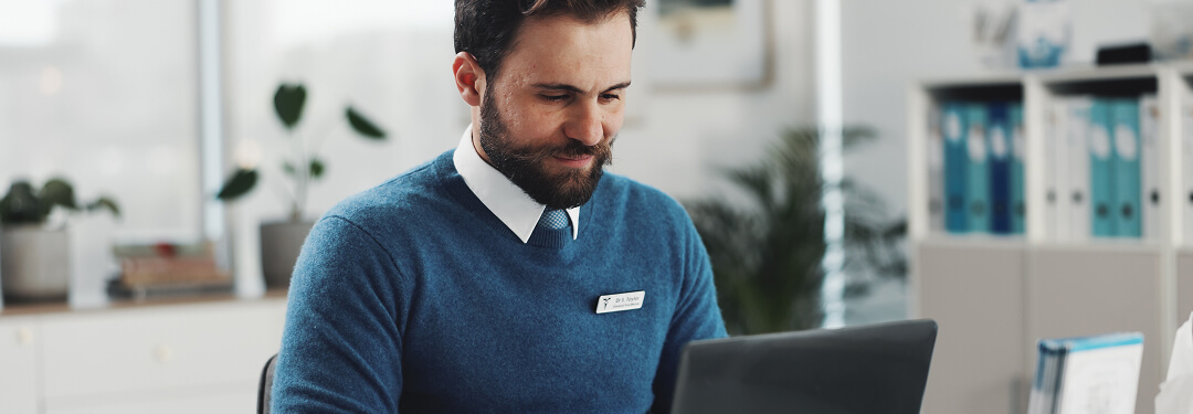 A doctor is typing on his laptop, exploring Medicaid updates and their implications for clinics.