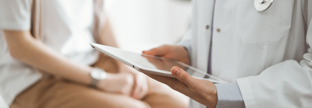 A doctor holds a tablet while a patient sits in the background, highlighting the role of AI in healthcare and trust.