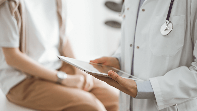  A doctor holds a tablet while a patient sits in the background, highlighting the role of AI in healthcare and trust.