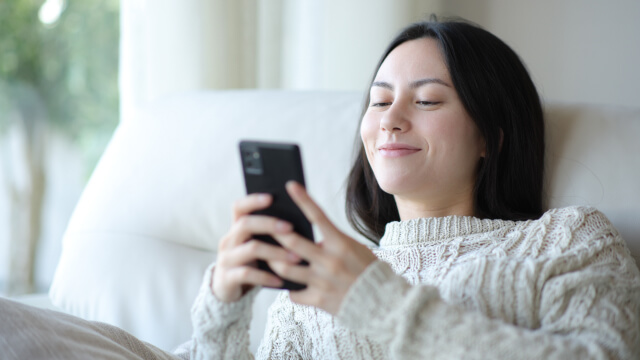 A patient sits on a couch using her phone, highlighting an improved patient experience with NextPatient.