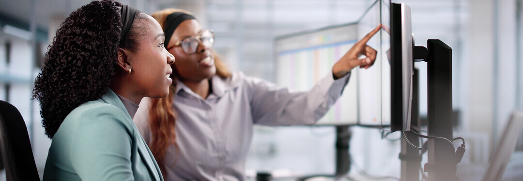 Two admins are working together in an office on a computer to enhance claim management efficiency.